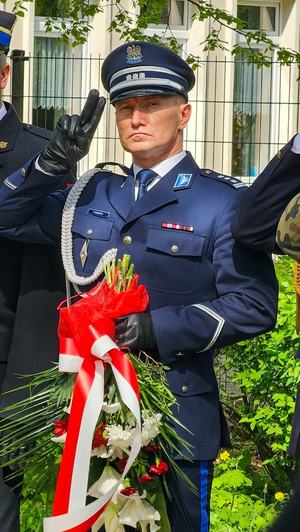 Komendant powiatowy w galowym mundurze z wiązanką kwiatów w dłoni.